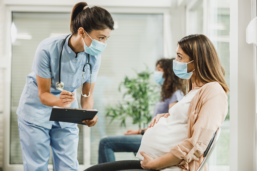 Mujer embarazada con máscara protectora hablando con la enfermera en la sala de espera photo