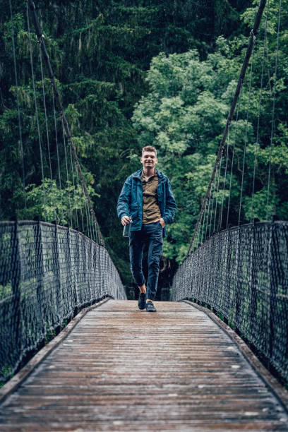 istock Young man hikes along suspension bridge in the rain 1340931748