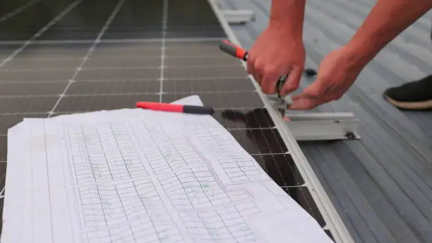 Photo of Close up of worker installing and working on maintenance of photovoltaic panel system installed. In the foreground is a diagram of the installation of solar panels. Solar panels on roof top