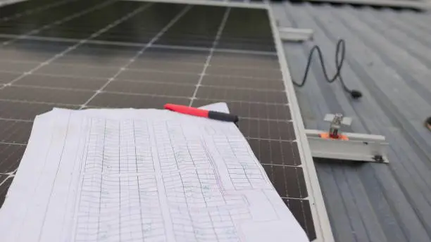 Photo of Close up of worker installing and working on maintenance of photovoltaic panel system installed. In the foreground is a diagram of the installation of solar panels. Solar panels on roof top