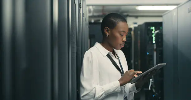 Photo of Shot of a young woman using a digital tablet while working in a data centre