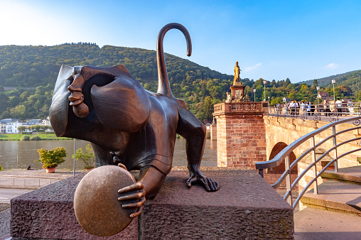 Heidelberg Bridge Monkey statue at Heidelberg Old Bridge, Germany. \nUpon the wish of the association Alt-Heidelberg, Gernot Rumpf designed a bronze statue of the monkey with a hollow head in 1977. It was then installed at the Old Bridge next to the tower in 1979. In contrast to its predecessors, the monkey’s right hand does not grasp its posterior, but shows the sign of the horns, which is supposed to ward off the evil eye.