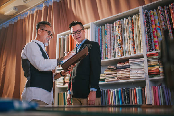 istock asian chinese senior man tailor write down record figure with digital tablet with his client's body size for new blazer making at studio and 1340940020