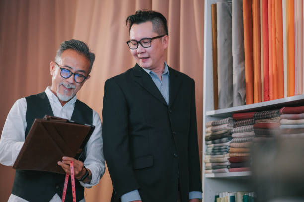 istock asian chinese senior man tailor write down record figure with digital tablet with his client's body size for new blazer making at studio 1340940143