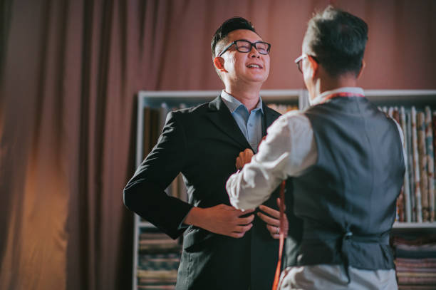アジアの中国の先輩男性は、彼のスタジオで新しいテーラードブレザースーツを試着して彼のクライアントを助ける仕立て - boutique retail new elegance ストックフォトと画像