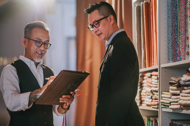 istock asian chinese senior man tailor write down record figure with digital tablet with his client's body size for new blazer making at studio 1340940233