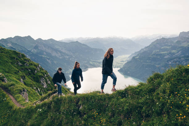 Friends hike up grassy mountain ridge at sunrise European Alps over lake Lugano in the distance switzerland photos stock pictures, royalty-free photos & images