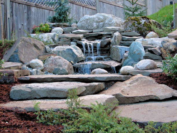 Garden Waterfall A garden waterfall built with mostly slabs of sandstone and surrounded by some granite boulder - rocks carefully placed into the existing hillside with flowing water. hardscape photos stock pictures, royalty-free photos & images