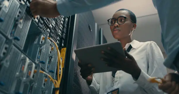 Photo of Shot of a man and woman using a digital tablet while working in a data centre