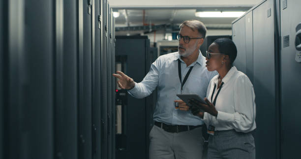 foto de un hombre y una mujer usando una tableta digital mientras trabajan en un centro de datos - data center computer programmer women fotografías e imágenes de stock