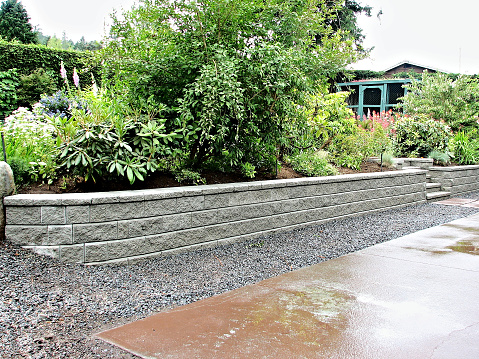 Gray block wall incorporated into an existing garden landscape replacing an old deteriorating wooden one for long lasting trouble free solution.