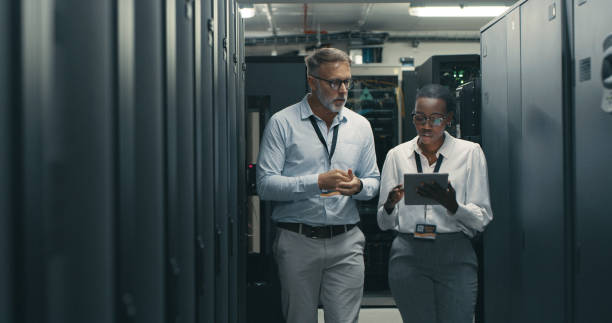 aufnahme eines mannes und einer frau mit einem digitalen tablet bei der arbeit in einem rechenzentrum - data center computer programmer women stock-fotos und bilder