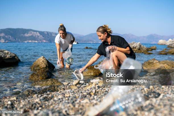 Two Volunteer Women Collect Discarded Plastic Waste By The Sea Stock Photo - Download Image Now