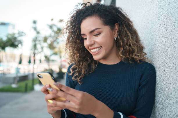 istock Latin woman smiling while using a mobile phone outdoors on the street. 1340955289