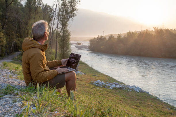 Man working on laptop relaxes near river at sunrise