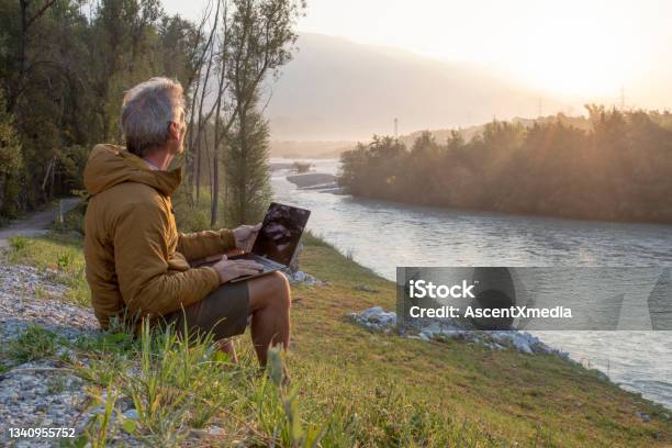 Man Working On Laptop Relaxes Near River At Sunrise Stock Photo - Download Image Now