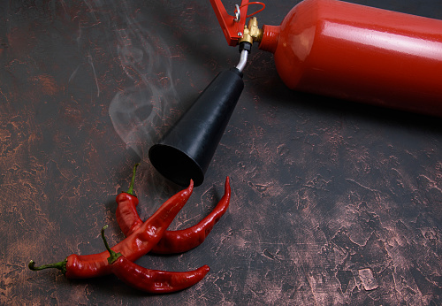 red bitter peppers on a black-copper wooden table , there is a little smoke , steam, a fire extinguisher is lying next to it, a concept