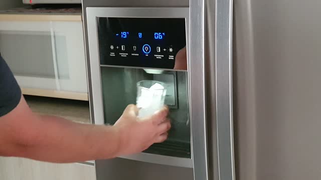 Man grabing ice cubs at refrigerator dispenser.