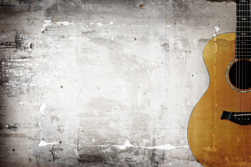 Acoustic guitar overlaid on a grungy concrete surface. Desaturated. Copy space. 