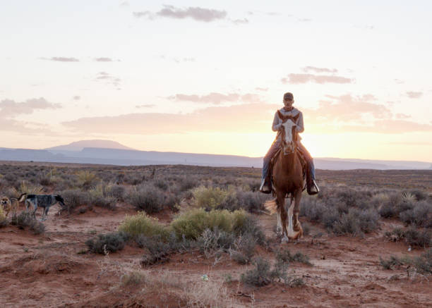 adolescenti e bambini navajo nativi americani che cavalcano cavalli insieme nella monument valley arizona, utah al crepuscolo sotto un tramonto drammatico alla fine dell'estate nel parco tribale - western usa foto e immagini stock