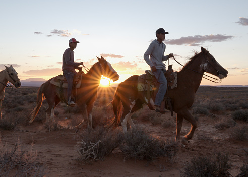 Native american navajo teenagers and children riding horses together in Monument Valley Arizona, Utah at dusk under a dramatic sunset in the late summer on the tribal park