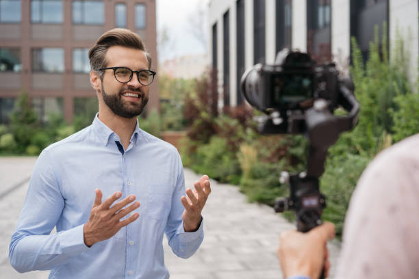 journalist oder nachrichtenreporter, der auf der straße sendet. tv-nachrichten, reportagekonzept. porträt eines selbstbewusst lächelnden influencers live-streaming - interview stock-fotos und bilder