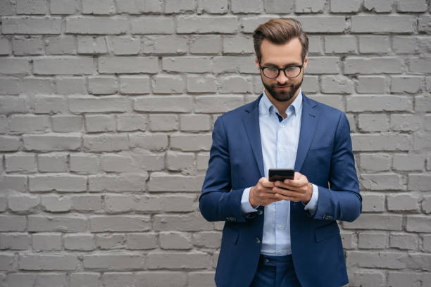 istock Man using mobile phone, shopping online, text messaging standing near grey wall. E-commerce,  mobile banking concept 1340973886