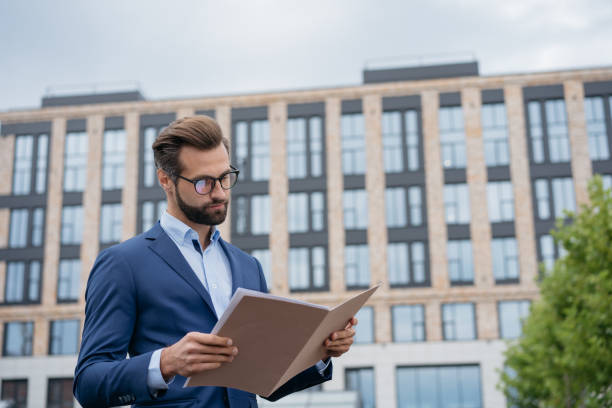 istock Businessman reading contract, analyzing documents. Young manager wearing stylish suit planning project, holding financial report 1340973966