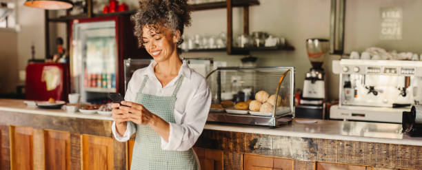 istock Cafe owner using a smartphone in her shop 1340975359