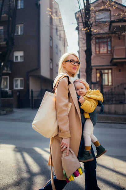 une mère avec une petite fille en porte-bébé se promène dans la ville - mother family vertical flower photos et images de collection