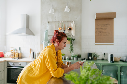 Photo of a mature woman using smart phone in a kitchen of her apartment