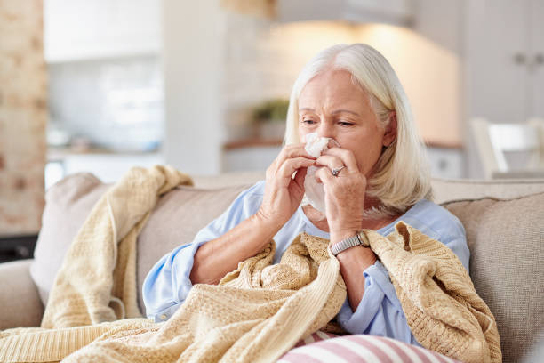 Shot of a senior woman blowing her nose while feeling sick at home stock photo