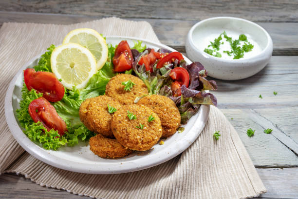 Fresh falafel from spiced chickpeas with lettuce salad, tomatoes, lemon slices and a yogurt dip on a rustic gray wooden table, selected focus stock photo