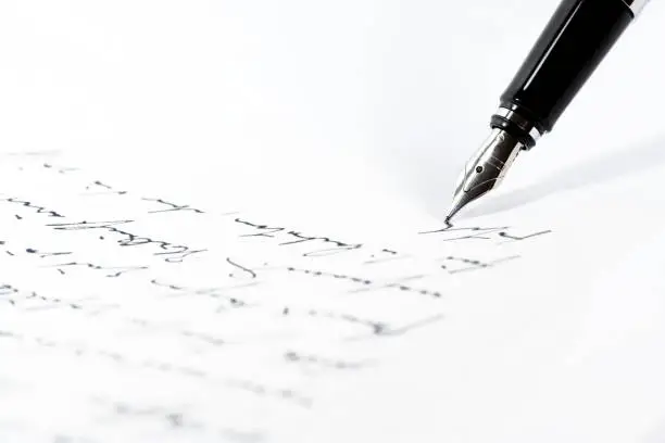 Photo of Black fountain pen is writing a letter or a manuscript on a white paper, copy space, close-up shot with selected focus
