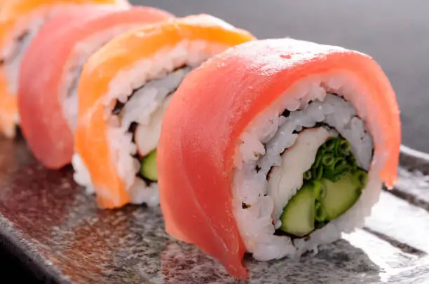 Salmon and tuna sushi roll on a black plate.