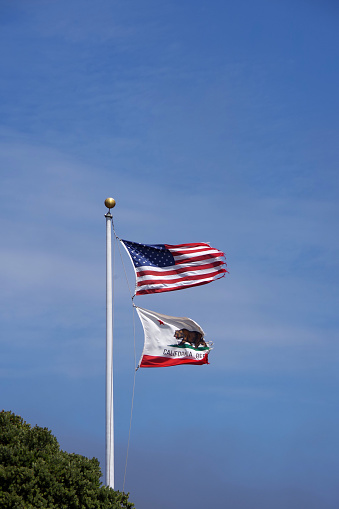 The US and California flags waving high in the wind under blue sky