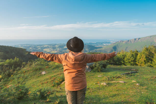 istock Unrecognizable woman standing on green grass with open arms looking at mountains under blue sky. freedom concept. 1340994876