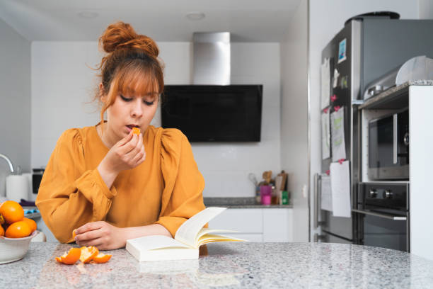 istock Caucasian woman eating a tangerine while reading a book on a table 1340994918