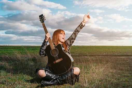 A woman sitting in a park holding a black guitar excited about the sight