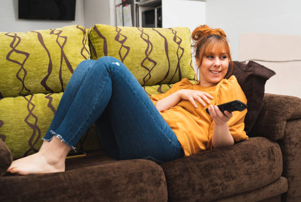 istock Caucasian female lying on a couch changing the channel with a remote 1340994938