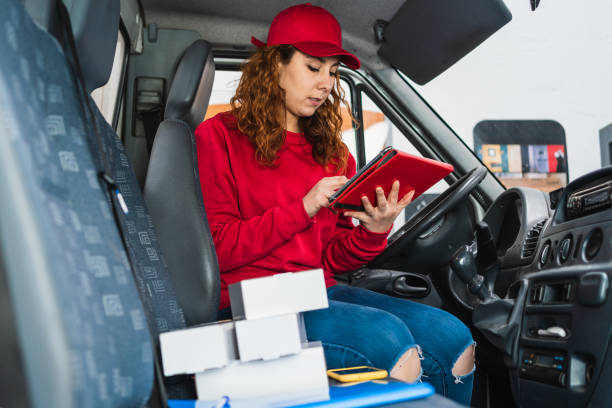 istock Female delivery driver tracking packages on a tablet in the van dressed in red 1340995135