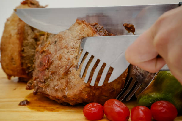 slice of pot cooked meat on wooden board with knife and cutlery.