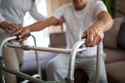 Man using walking frame with assistance of his wife at home, close up, focus on hands