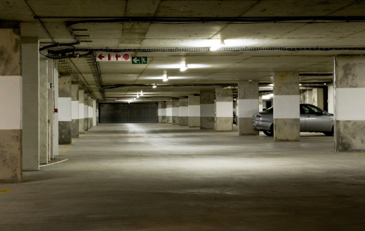Lit by the sickly glow of cheap fluorescent tubes, an underground parking garage stands almost empty late at night. One car is left.