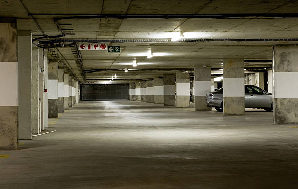 Underground parking garage Lit by the sickly glow of cheap fluorescent tubes, an underground parking garage stands almost empty late at night. One car is left. suspicion photos stock pictures, royalty-free photos & images