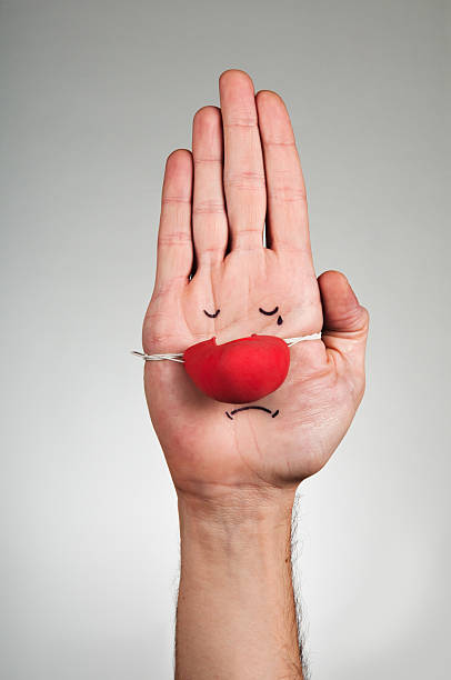 Hand with red rubber nose and sad face painted stock photo