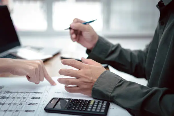 Photo of Engineering work concept : Close up hand a man meeting action and use pencil calculator in Calculating drawing and document on the wood table