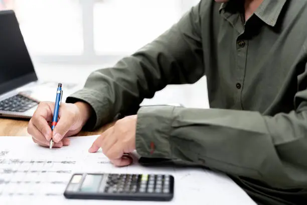 Photo of A man use pencil write in drawing in engineering work  with calculator paint chart and drawing on table