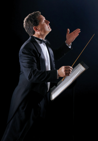 A photo of a music conductor wearing a tuxedo, conducting an orchestra on a black background