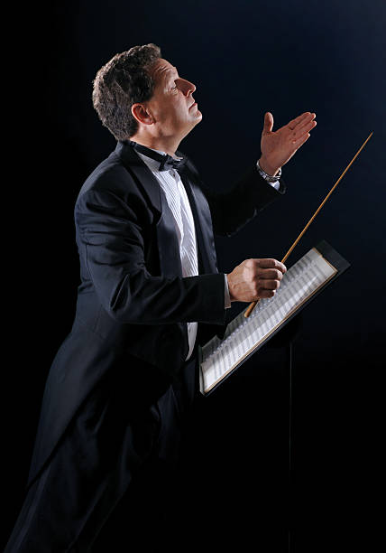 The Music Conductor A photo of a music conductor wearing a tuxedo, conducting an orchestra on a black background conductors baton photos stock pictures, royalty-free photos & images